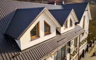 Close-up aerial view of building attic rooms exterior on metal shingle roof, stucco walls and plastic windows.