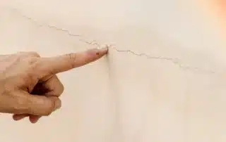 Damaged plaster wall showing cracks and surface deterioration being inspected for repair and restoration