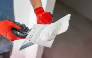 A damaged stucco wall being skillfully patched by a contractor in a sunny Florida setting.