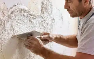 A skilled contractor meticulously applies stucco patch to repair cracks on a home's exterior.